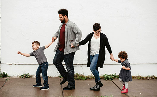 family of 4 holding hands and marching down sidewalk in a line